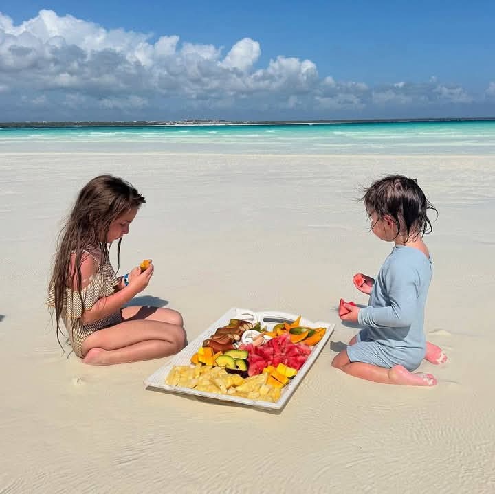 Children enjoying a fruit platter on a sandbank in turquoise water